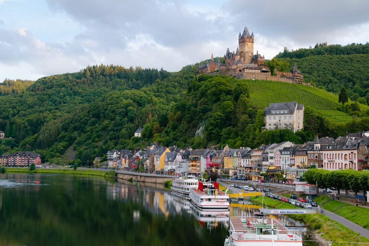 Boats on water and houses next to water with castle up on a hill
